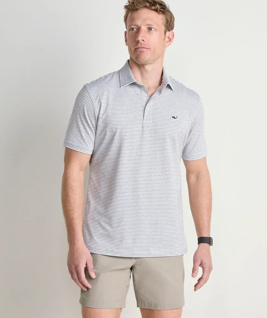 Man wearing Vineyard Vines Bradley Stripe Sankaty Polo, a striped polo shirt and beige shorts on a plain background