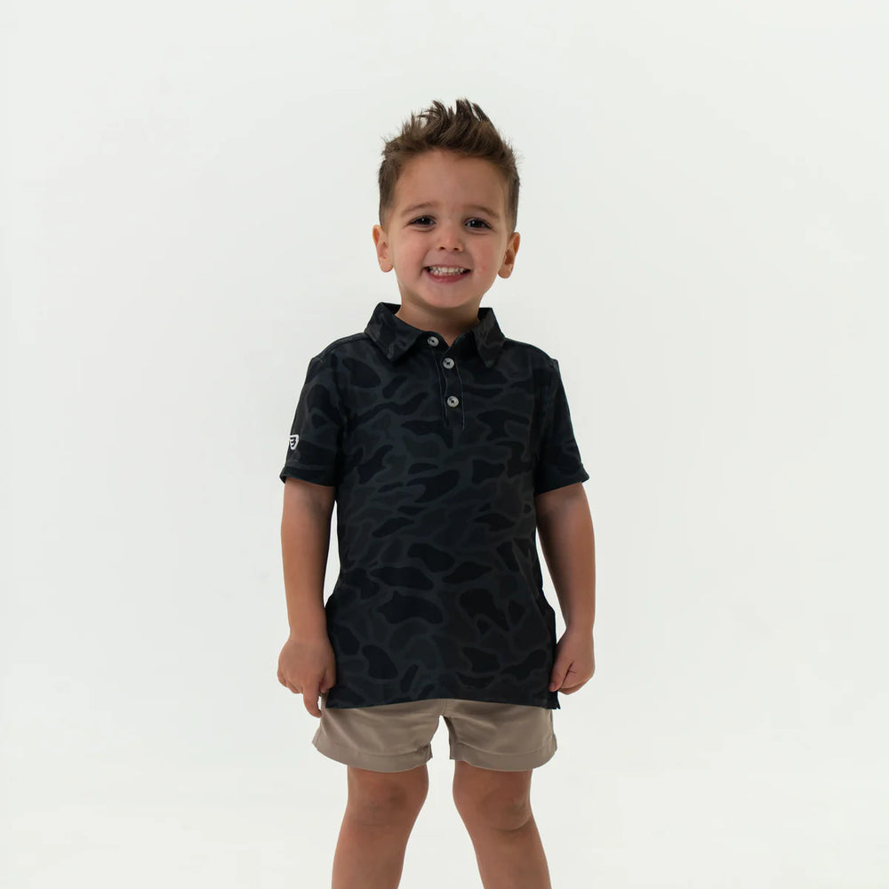Child wearing Burlebo Youth Performance black patterned polo shirt and beige shorts for school, play, or outdoor adventures.