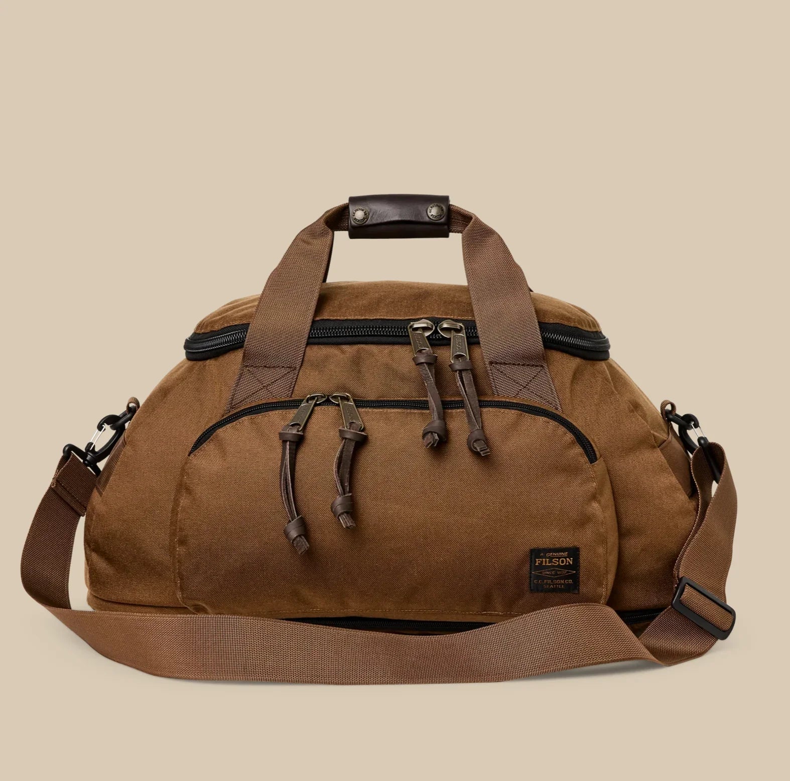 Filson Dryden Duffle Pack in tan with zippered compartments, leather accents, and convertible duffle‑to‑backpack straps.