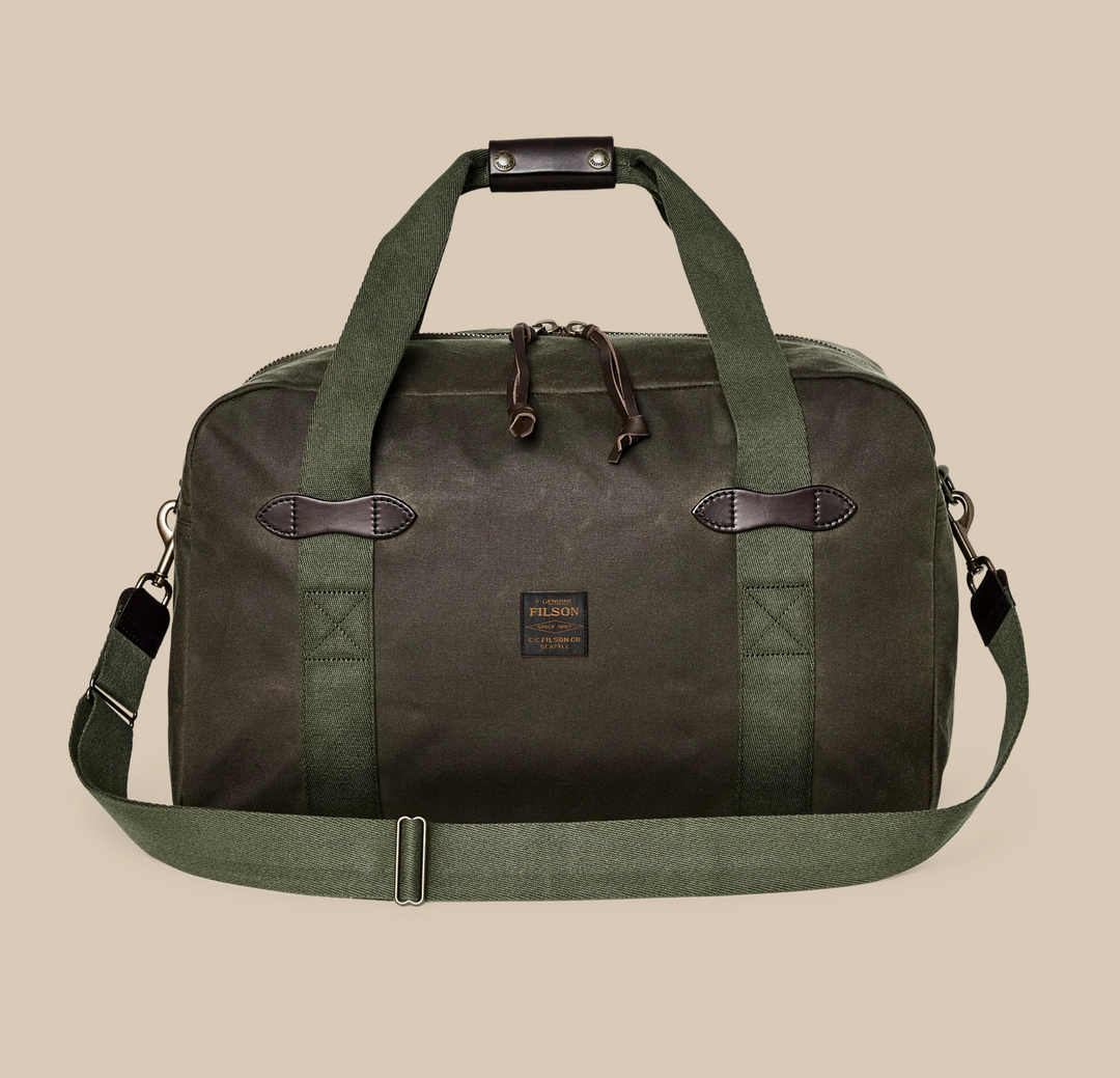 Filson TIn Cloth Medium Duffle in dark brown with zippered compartments, leather accents, and convertible duffle‑to‑backpack straps.