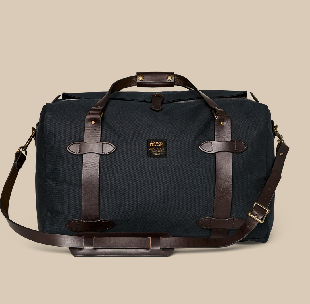 Filson Rugged Twill Medium Duffle Waterproof Leather Back Pack in black with zippered compartments, leather accents, and convertible duffle‑to‑backpack straps.