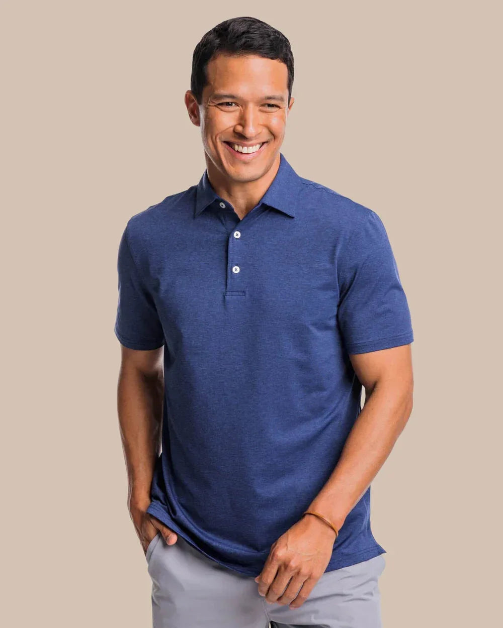 Man wearing Southern Tide Breeze Performance Heather Blue  Polo shirt against a beige background